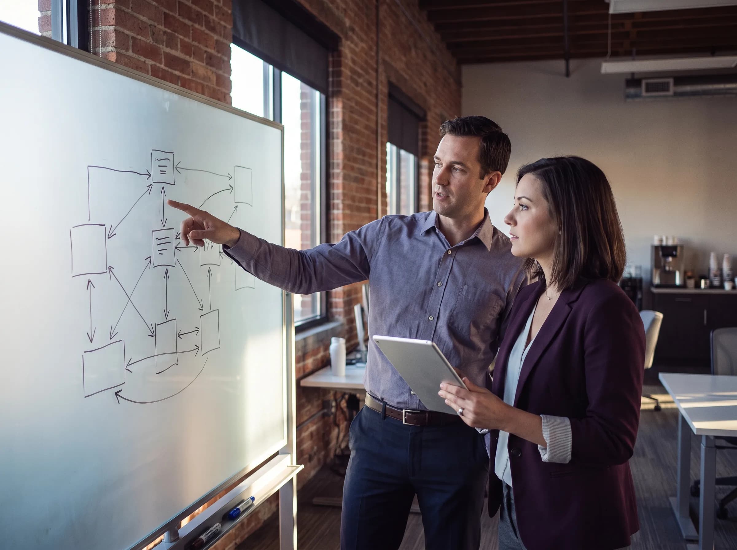 Two software architects reviewing a system architecture diagram on a whiteboard